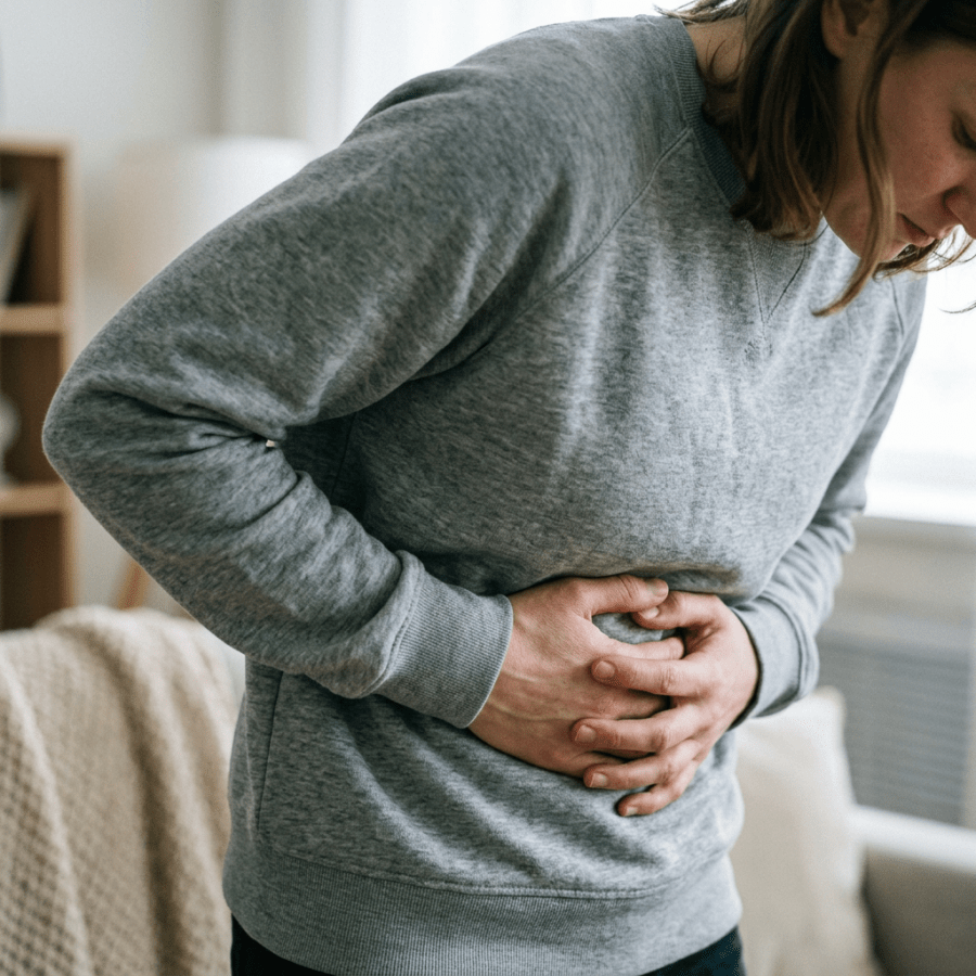Person holding abdomen, appearing in pain, wearing grey sweatshirt