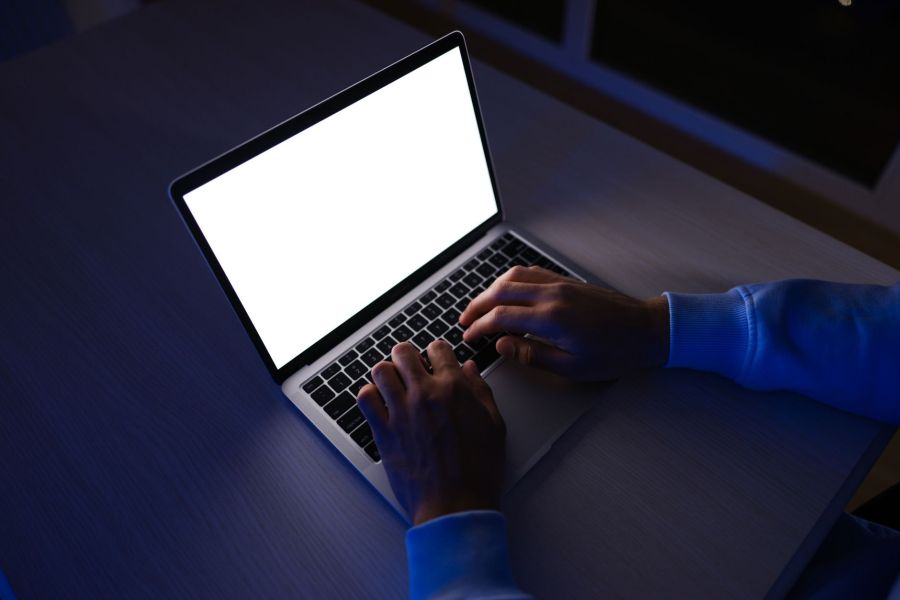 Hands typing on a laptop with a bright blank screen in a dark room at night