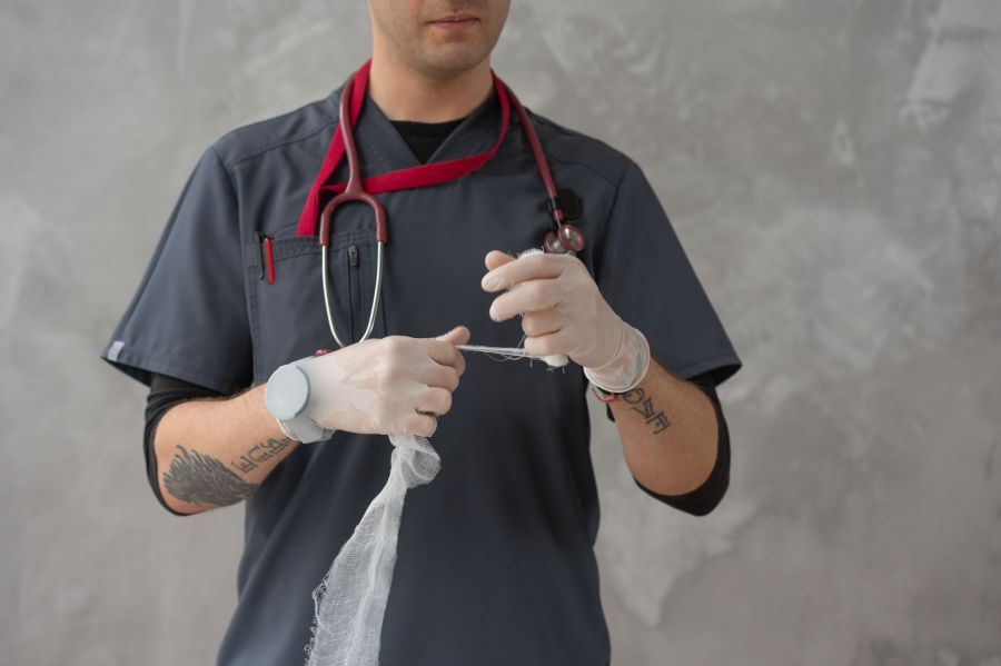 A clinician in scrubs and gloves preparing a length of sterile gauze for a dressing.